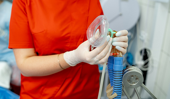 Dental team member with gloved hands holding mask for nitrous oxide sedation