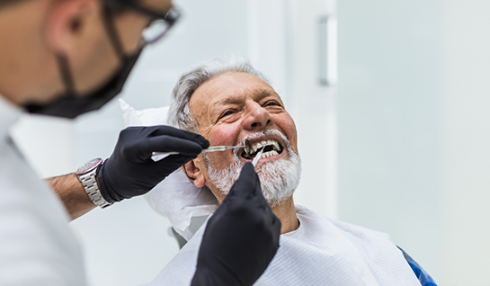 Older male dental patient having teeth examined by dentist