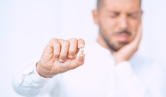 Man rubbing jaw and holding extracted tooth