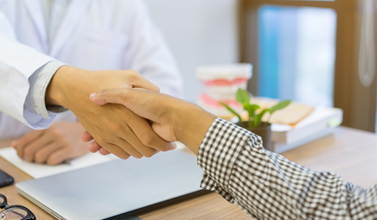 Shaking hands over desk with laptop