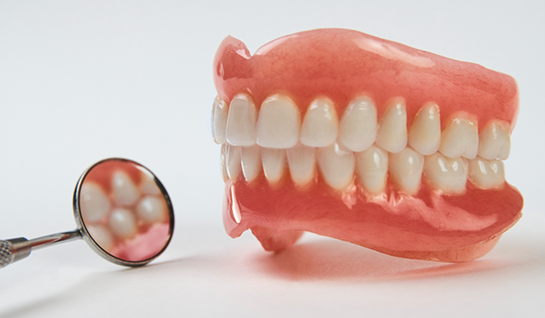 Dentures sitting next to dental mirror