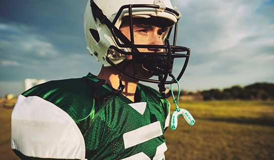 Boy with football helmet with mouthguard dangling off it